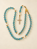 Blue quartz rosary laid out on warm ivory with the gold-tone baguette CZ cross