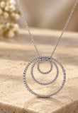 14K white gold three concentric diamond circles necklace on warm stone background, standalone featured product image